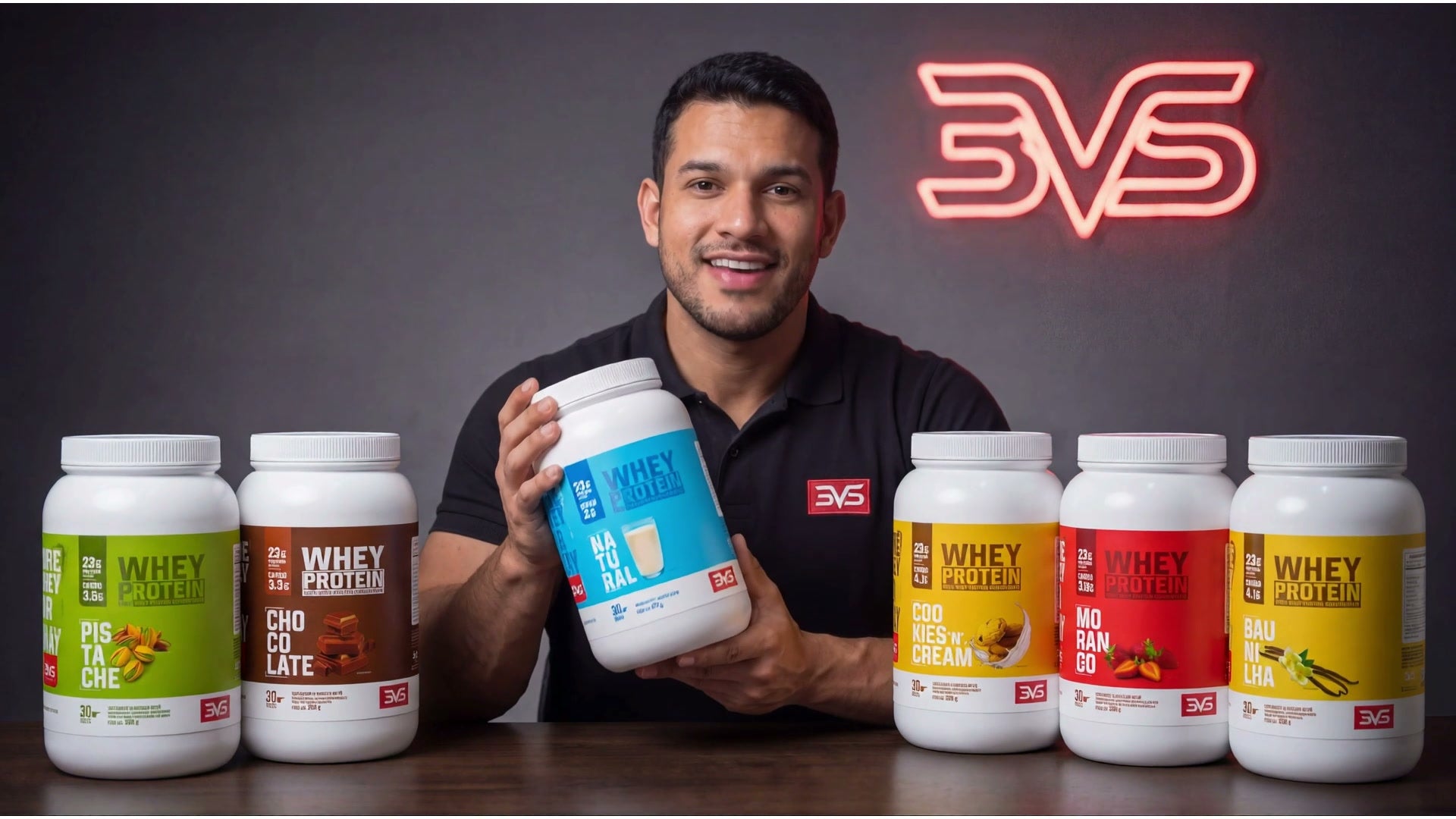 Apresentador segurando um pote de Whey Concentrada 3VS diante dos sabores da linha